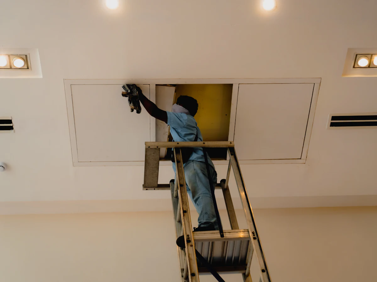 Techniker auf einer Leiter arbeitet an einer Revisionsklappe in der Decke